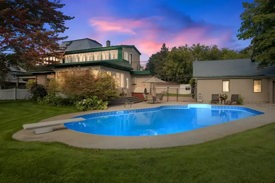 The lit pool behind the two-story house at dusk, with a pink sky over the trees